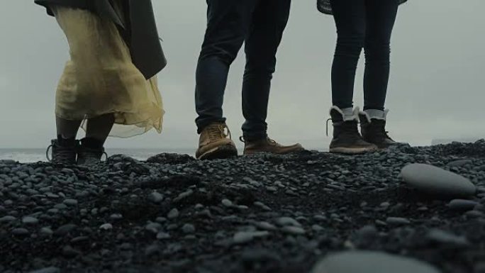 站在冰岛黑色火山海滩上的人们脚的特写镜头。探索岛屿的游客
