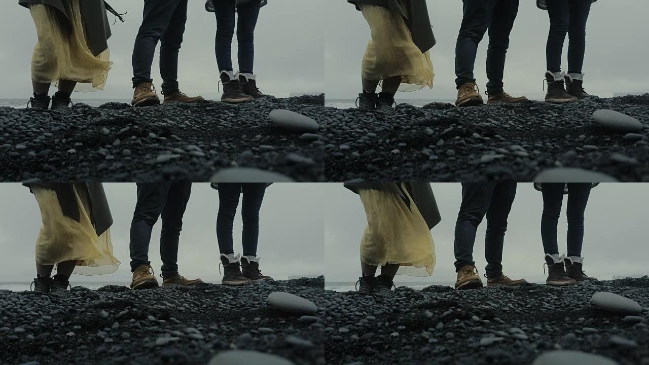 站在冰岛黑色火山海滩上的人们脚的特写镜头。探索岛屿的游客