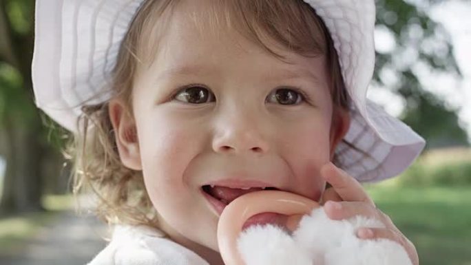特写，dop: 开朗的小女儿在咀嚼蓬松的玩具时微笑