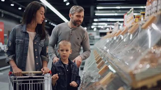 幸福的家庭妈妈，爸爸和可爱的孩子正在大型超市中选择食物，指着塑料容器，说话，微笑和大笑。人和购物概念