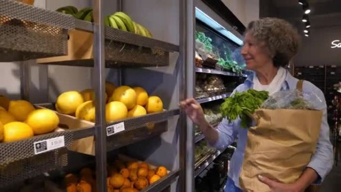 高级妇女在有机食品市场购物，看着货架上的食品价格并选择水果