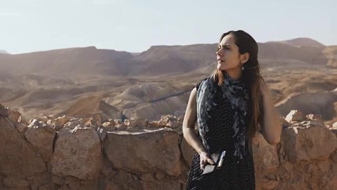 背着背包的女孩看着山全景。迷人的欧洲女人探索古老的废墟。以色列马萨达。4K