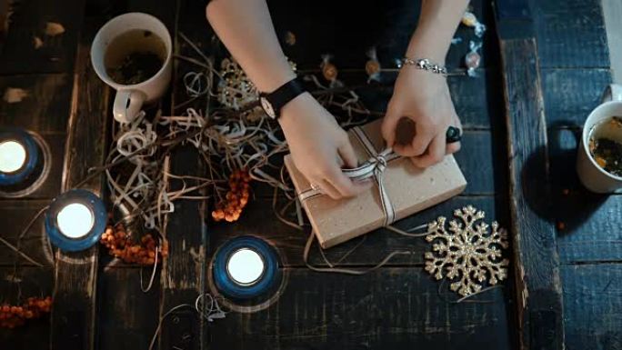 女性双手的顶部特写视图用缎带绑住盒子，装饰坐在桌子上的圣诞节礼物