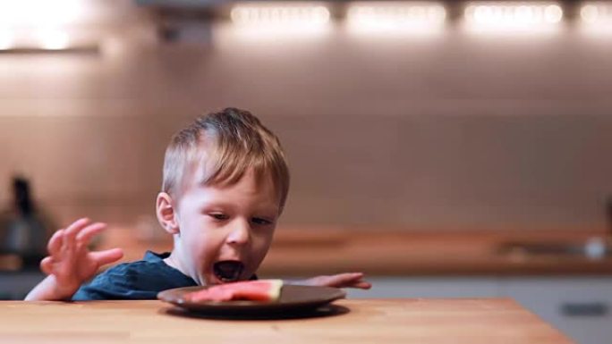 小男孩坐在桌子旁，转过头，看到盘子里有西瓜。男性欢呼雀跃，咬一口