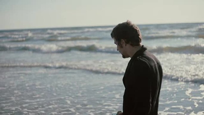 一个年轻人在大风天沿着美丽的海滩散步，手里拿着运动鞋