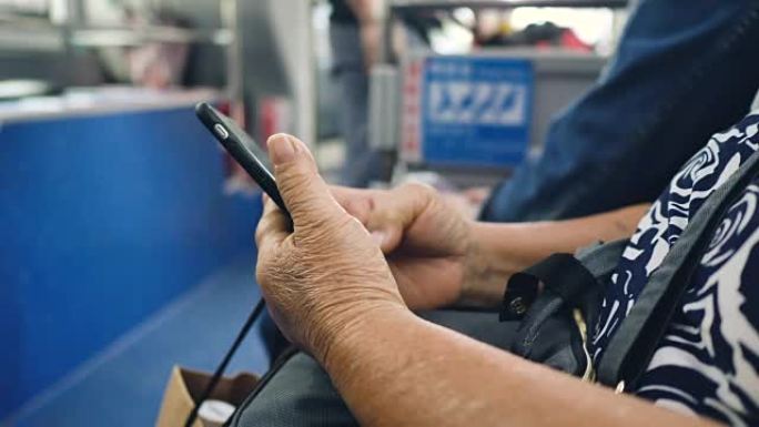 老年妇女在公共汽车上的乘客座位上使用智能手机