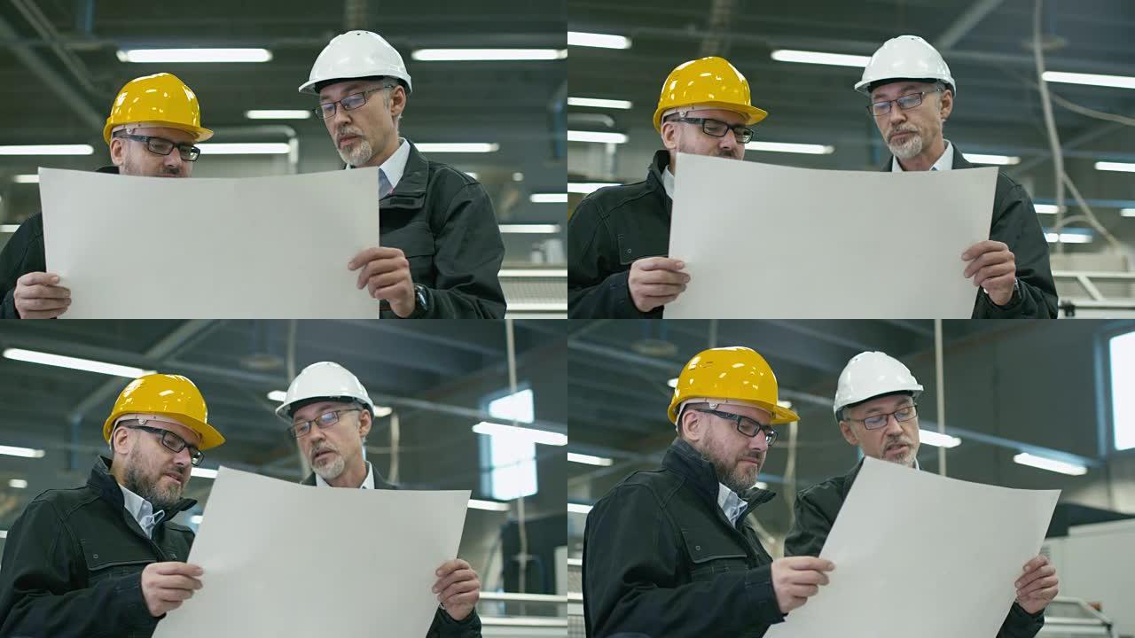 两名戴着安全帽的工程师站在工厂里讨论蓝图。
