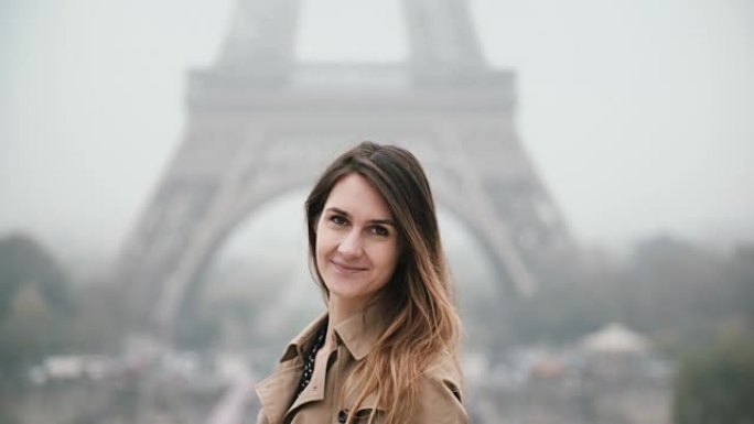年轻漂亮的女人站在法国巴黎的埃菲尔铁塔附近，转身看着相机，微笑着