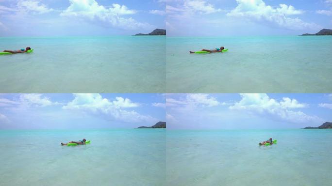 快乐的年轻女子在蓝色比基尼躺和享受充气床在热带海洋在美丽的异国情调的岛屿在她的暑假