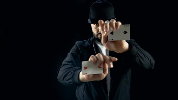 戴着帽子的专业街头魔术师表演令人印象深刻的手牌技巧。背景是黑色的。