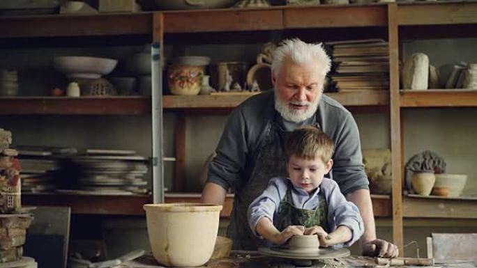 集中的孩子在他经验丰富的祖父的指导下，用陶工轮上的粘土形成锅。背景是陶瓷罐，花瓶和人物。