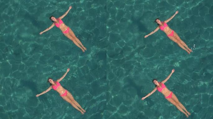 空中: 轻松的年轻女子在清澈的海洋泻湖中游泳和漂浮