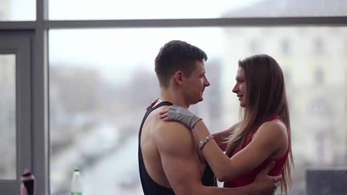 年轻夫妇互相表达爱意。爱中的运动男人和女人拥抱和亲吻站在窗户附近