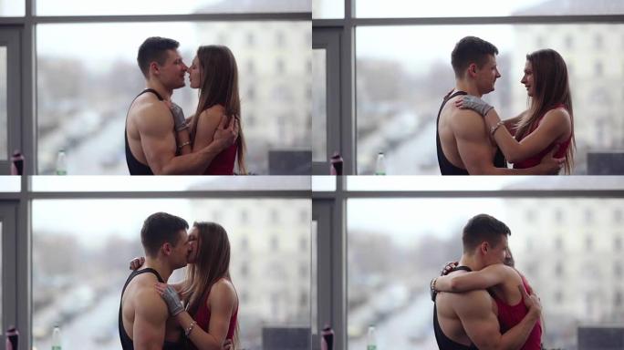 年轻夫妇互相表达爱意。爱中的运动男人和女人拥抱和亲吻站在窗户附近
