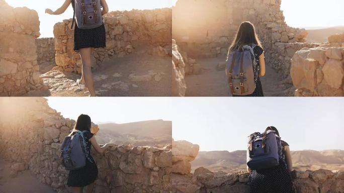 背着背包的女孩探索古老的沙漠废墟。漂亮女人走在以色列马萨达的山堡垒城墙之间。4K