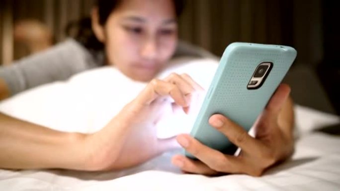 快乐的年轻亚洲女性在床上使用智能手机。