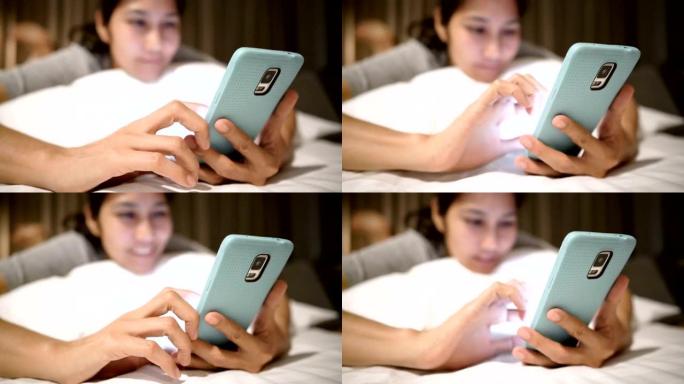 快乐的年轻亚洲女性在床上使用智能手机。