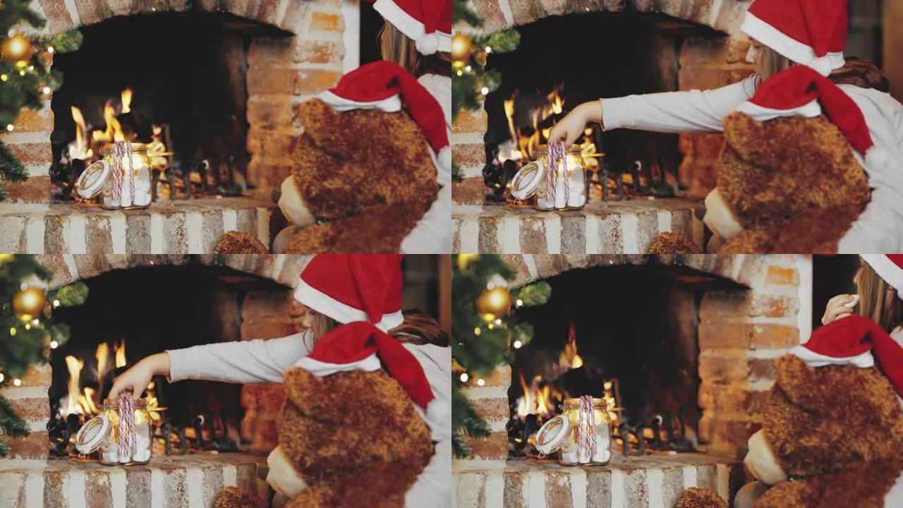 4k女孩和泰迪熊戴着圣诞老人帽子，在壁炉旁吃棉花糖，实时