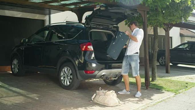 慢动作: 快乐的男性将行李放入一辆凉爽的现代SUV的后备箱中。