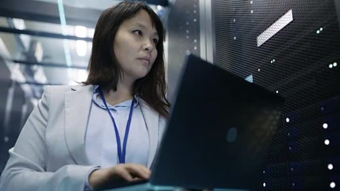 特写的女性亚洲IT工程师工作在一个笔记本电脑上的数据中心充满机架服务器。