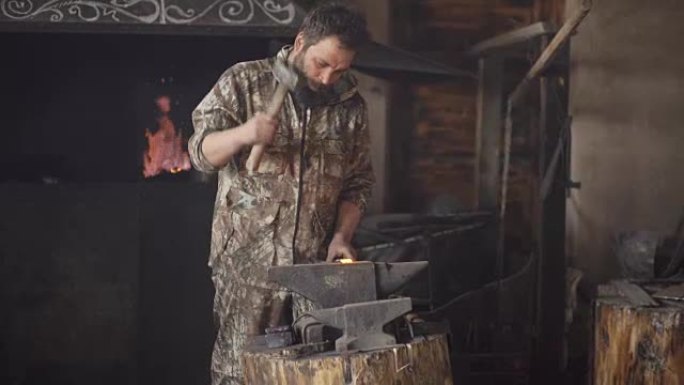 大胡子的年轻人铁匠用火花烟花在铁匠铺的铁砧上手工锻造铁水