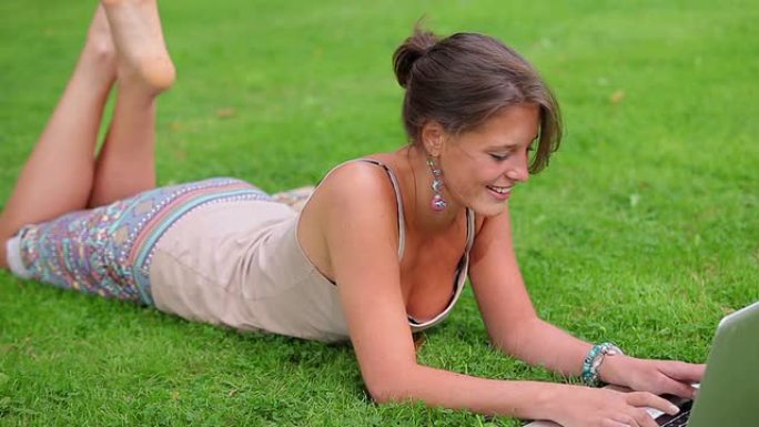 快乐的学生躺在草地上，用她的笔记本电脑