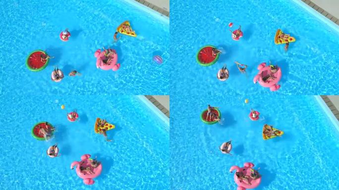 空中: 年轻顽皮的人在游泳池中充气的彩色浮标上玩乐