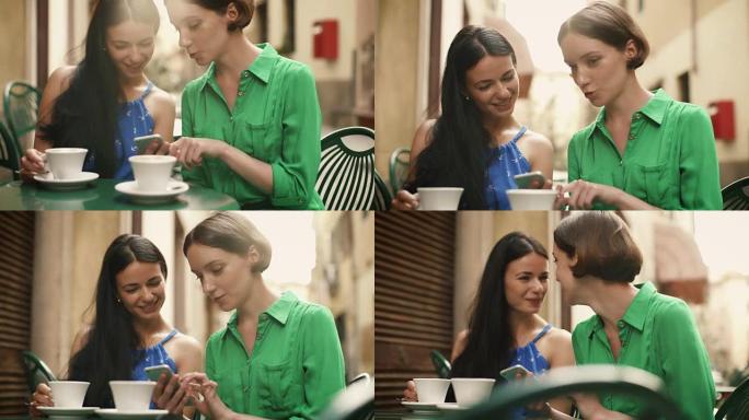 两个穿着浅色夏装的迷人年轻女性在街头咖啡店放松和交谈。一个人在手机上分享一些令人兴奋的东西。