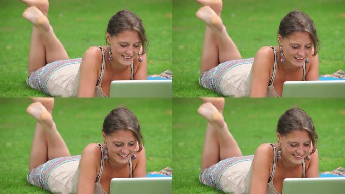 用笔记本电脑躺在草地上的漂亮学生