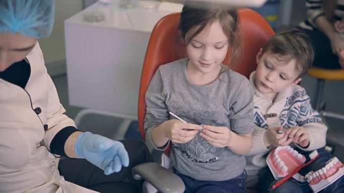 两个孩子在牙科检查前坐在牙医的椅子上。弟弟和妹妹和年轻的医生发霉