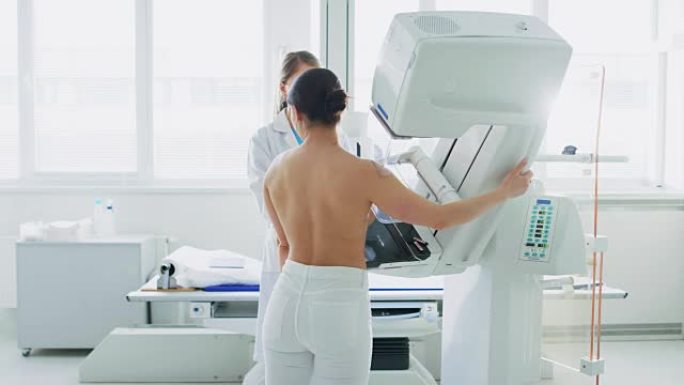 在医院，乳房x线照相术技术专家/医生按下乳房x线照相机上的按钮激活女性患者扫描。医生解释乳腺癌预防筛