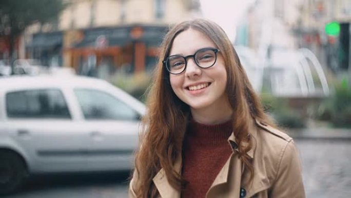 戴着眼镜看着相机喝茶的年轻微笑学生的肖像。快乐女人走在法国巴黎