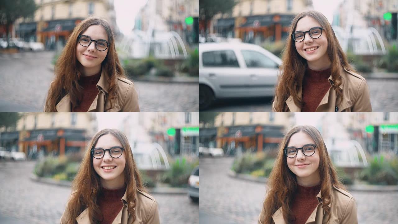 戴着眼镜看着相机喝茶的年轻微笑学生的肖像。快乐女人走在法国巴黎
