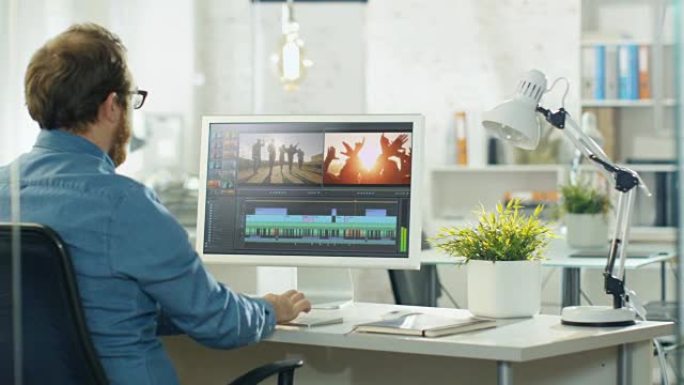 男性视频编辑器在带有两个显示器的个人计算机上处理镜头和声音。他在明亮的办公室阁楼工作。