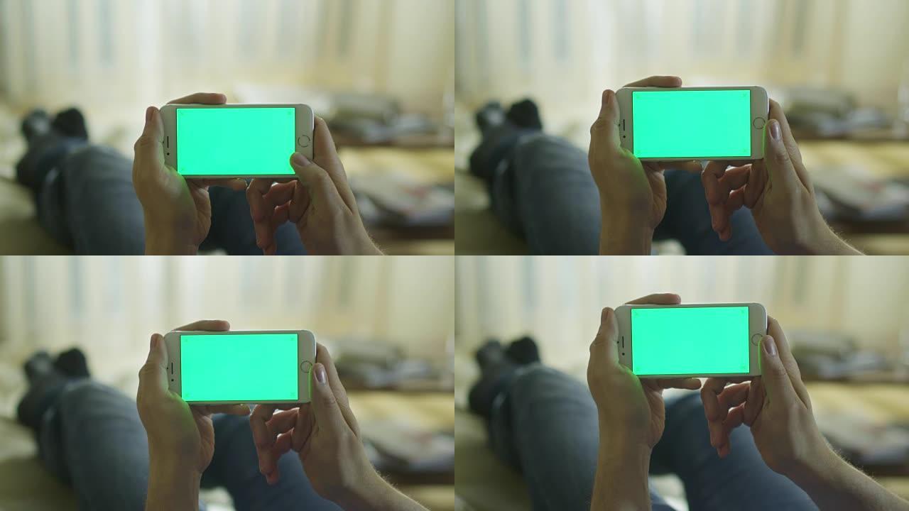 男人躺在家里的沙发上，在风景模式下使用绿屏手机。