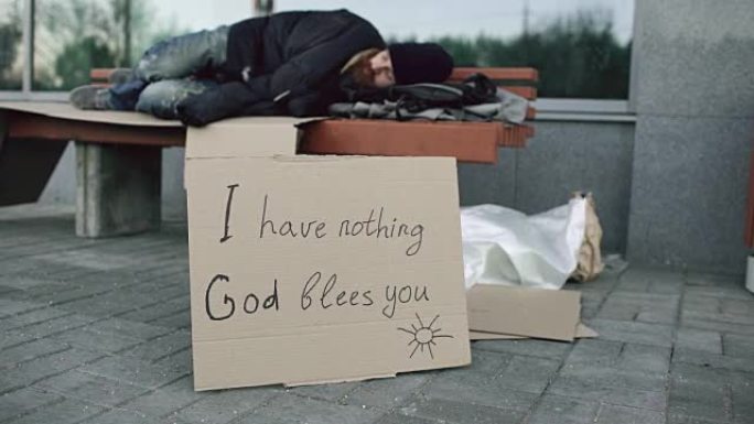 一个无家可归的年轻人睡在城市街道的长椅上
