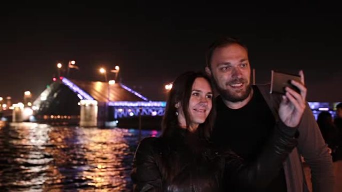 恋爱中的幸福情侣自拍。背景上的圣彼得堡可移动宫殿桥。夜间城市照明