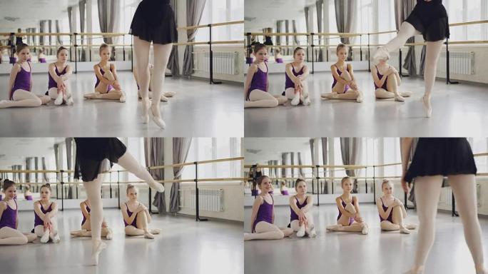 芭蕾舞老师专业芭蕾舞演员tip着脚尖跳舞，向坐在地板上看导师的小学生们展示动作。