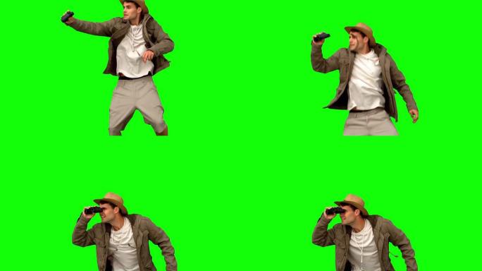 男子在绿屏上跳跃和使用双筒望远镜
