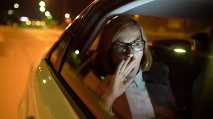 女士疲惫的女商人在夜间驾驶的汽车后座上打哈欠