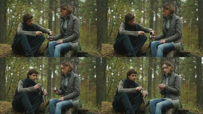 男人和女人坐在森林里的一块木头上喝茶。