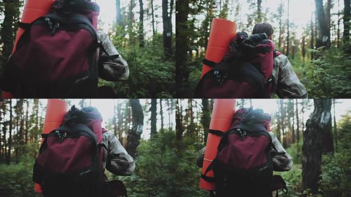 穿着迷彩服的年轻人的背景图，背着背包和旅游垫子独自在早晨穿过森林