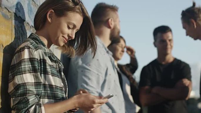 在城市环境中，一群青少年朋友在户外使用手机的迷人少女。