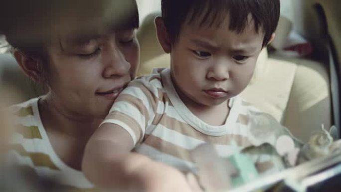 亚洲男婴读书与年轻的母亲乘车旅行。