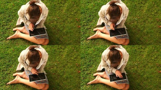 坐在草坪上使用平板电脑的学生
