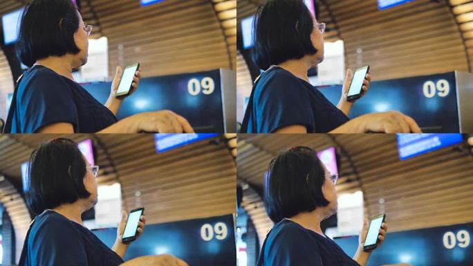 高级妇女在机场的智能手机上检查她的航班