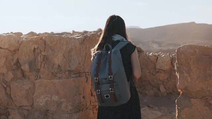 背着背包的女人走在古老的城墙之间。迷人的高加索女性游客喜欢山全景。马萨达。4K