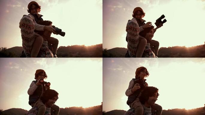 年幼的儿子在日落时用双筒望远镜帮助徒步旅行者的父亲