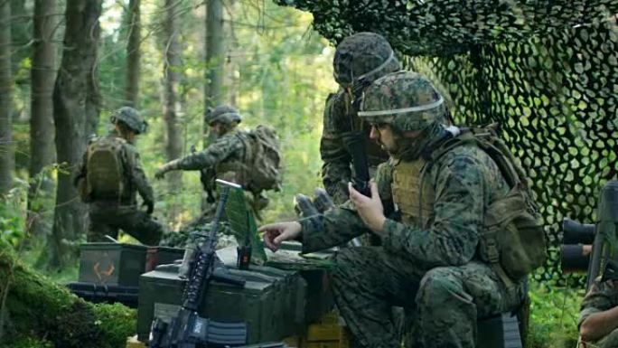 军事集结基地，军官向总工程师下达命令，他们使用无线电和军用笔记本电脑。他们在森林迷彩帐篷里。他们正在