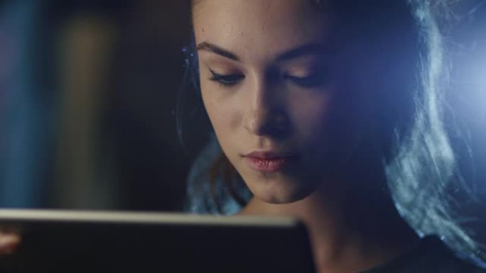 一个漂亮的年轻女孩在黑暗中拿着工作平板电脑的肖像照片。